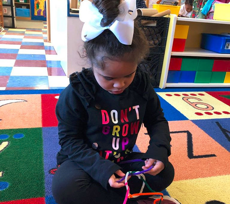 An african american young little girl trying to design a ring using colorful strings at a Christian Preschool & Daycare Serving Loganville, GA